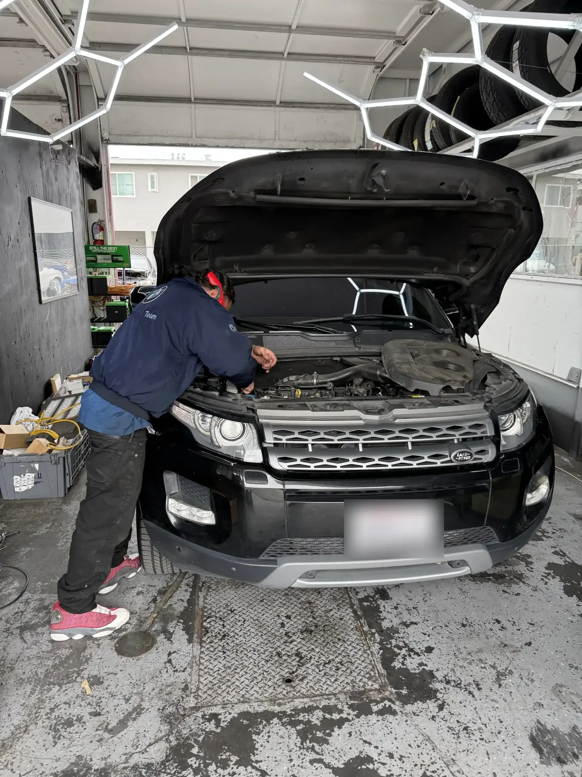 Beacon Auto Care technician Favio leaning into the engine bay of a black Range Rover Evoque diagnosing an AC fault at the San Mateo shop